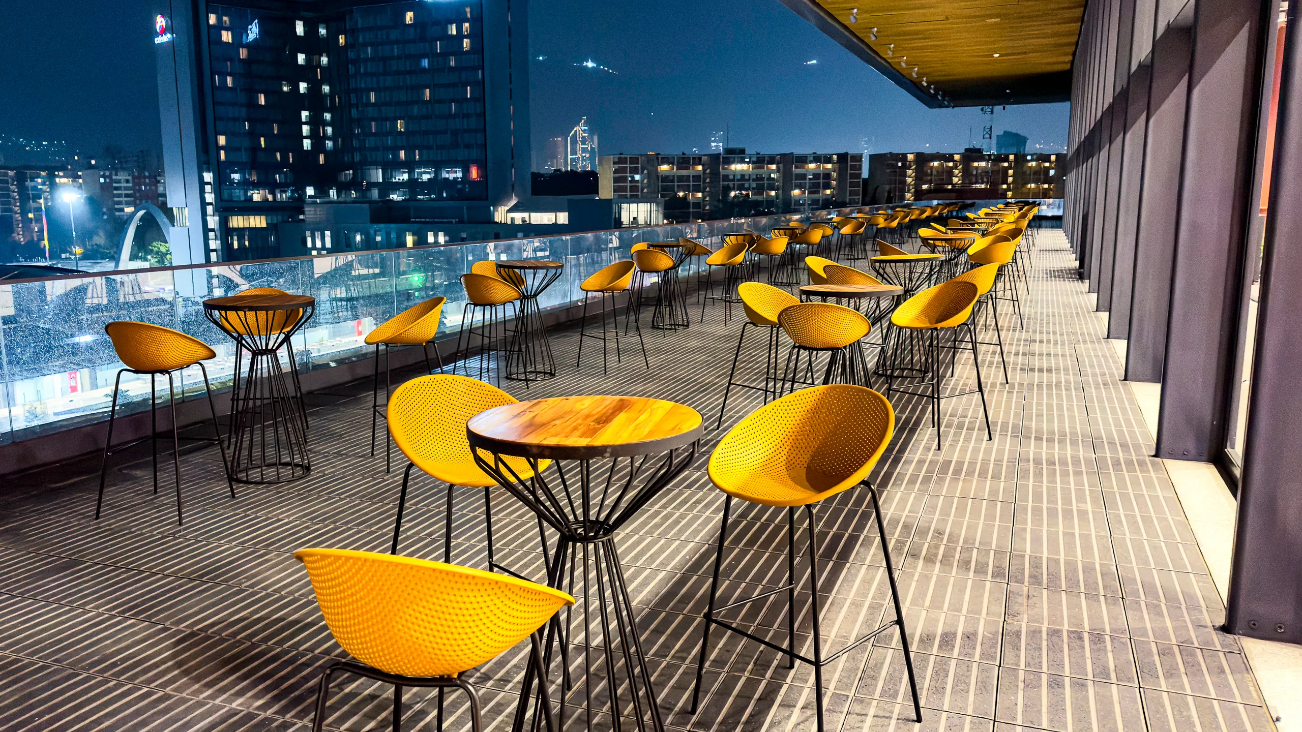 Terraza lounge con sillas altas y vista nocturna a la ciudad para evento